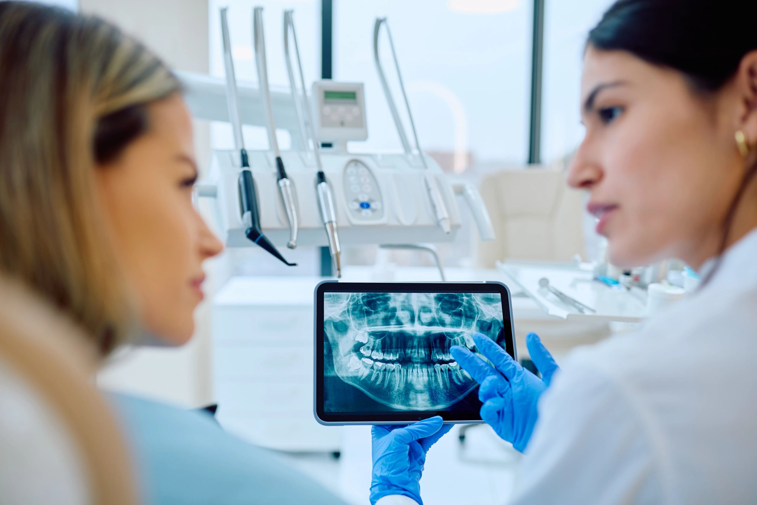 Dentist explaining dental X-ray to patient on tablet during implant consultation